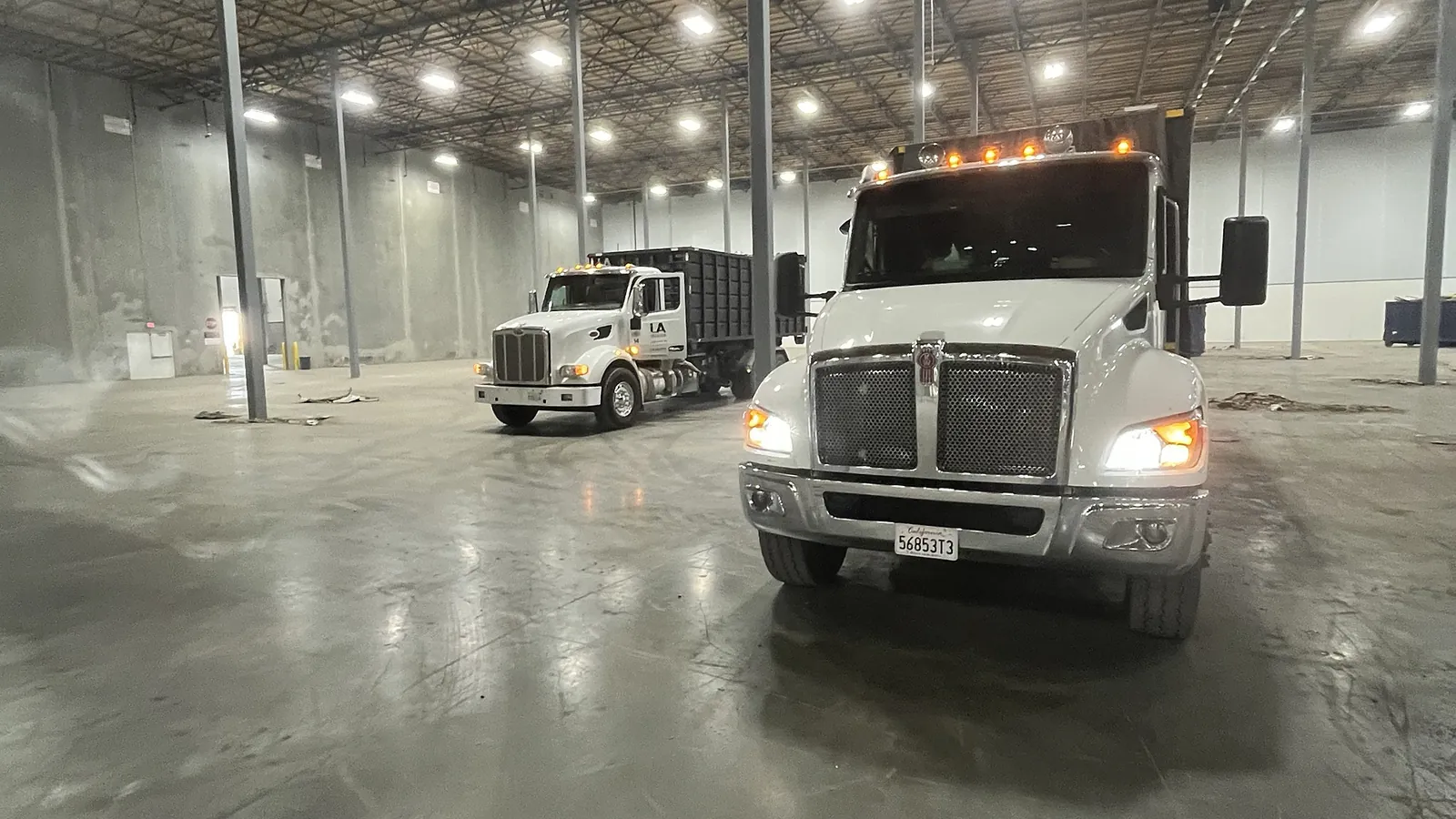 Two LA Waste roll off trucks inside a warehouse
